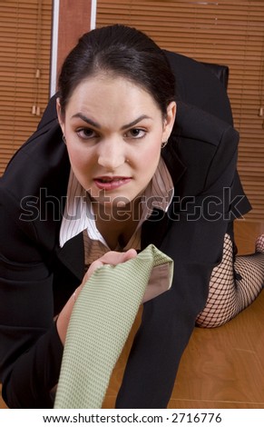 Brunette business woman with black suit crawling on desk holding green tie