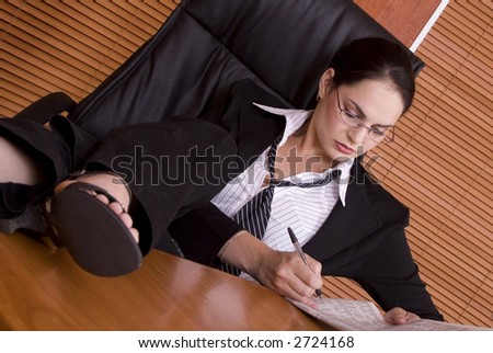 Brunette business woman with black suit with legs on desk reading financials