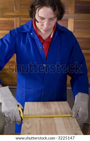 Dark haired man with blue overall measuring wood with gloves