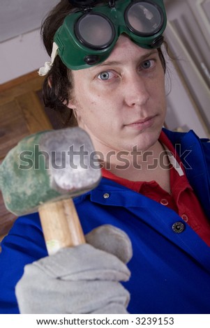 Dark haired man with blue overall holding hammer (focus on the handyman)