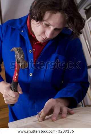 Dark haired man with blue overall hitting nail with hammer