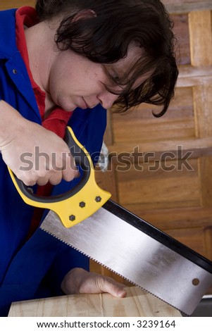 Dark haired man with blue overall holding saw with wooden board