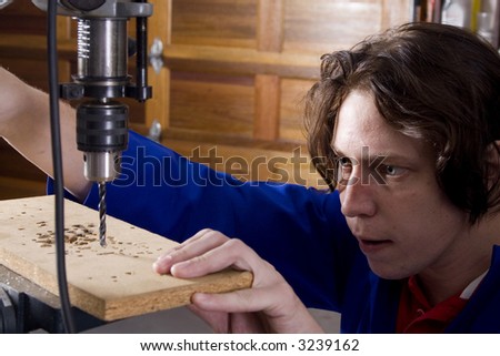 Dark haired man with blue overall using drill machine