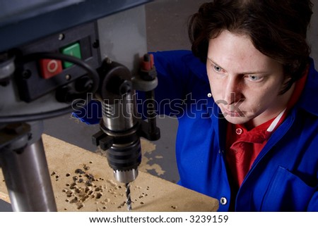 Dark haired man with blue overall using drill machine with focus on handyman