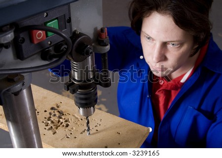 Dark haired man with blue overall using drill machine with focus on drill bit