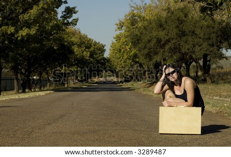 Brunette waiting roadside for a lift resting on suitcase with hands in hair