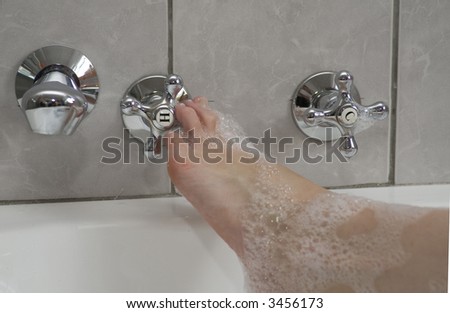 Woman\'s boot adjusting the hot water tap in a bubble bath