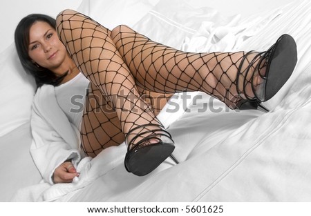 Attractive woman with bath robe on white bed with fishnet stockings and high heel shoes.