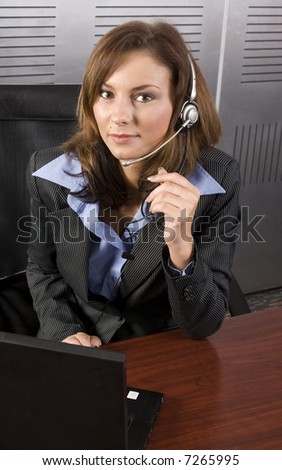 Young attractive brunette call center agent talking on the headset in a modern office setting with laptop