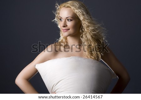 Attractive curly blond woman holding pillow across her naked body