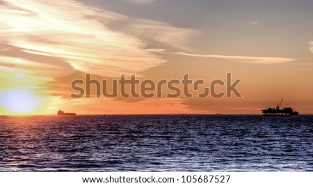 Scenic landscape off shore oil rig and cargo ship at sunset