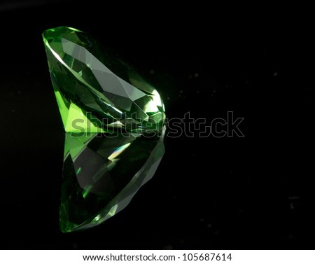 Emerald green round cut faceted gemstone on black background with reflection