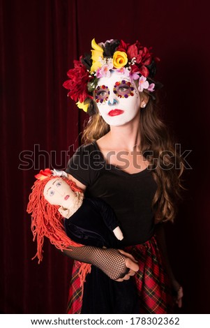 Day of The Dead girl in make up, costume, and headress holding creepy doll