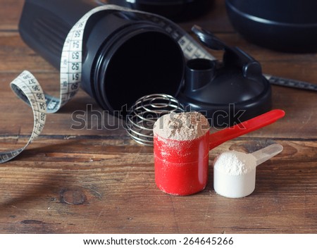 Whey protein powder in scoop with vitamins and plastic shaker on wooden background. Selective focus, shallow DOF