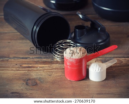 Whey protein powder in scoop with  plastic shaker on wooden background