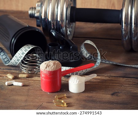Whey protein powder in scoop with vitamins and plastic shaker on wooden background. Selective focus, shallow DOF