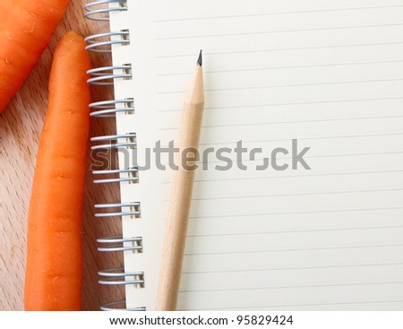 Directly above close-up view of a table with a Carrots and a notebook on cutting board