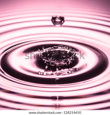 A water drop, in the shape of a heart, falls towards a splash made in a pool of water.