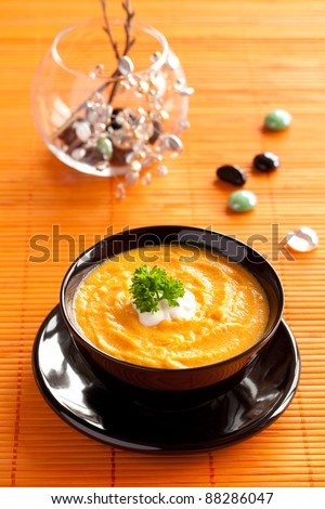 Pumpkin Cream Soup with leaf of parsley served in black dish on the orange table mat.