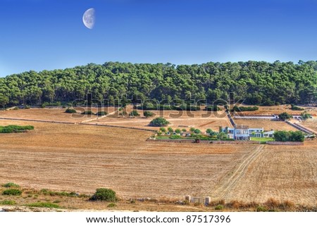 Menorcan farm with a blue sky with a large day moon with forest and woods in background