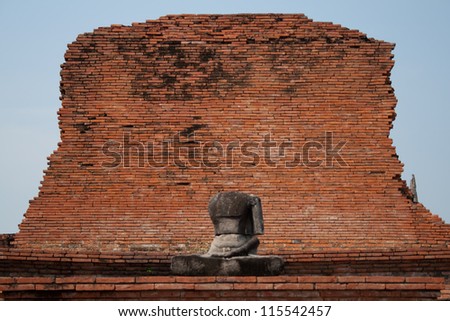 Buddha statue without head against a brick wall