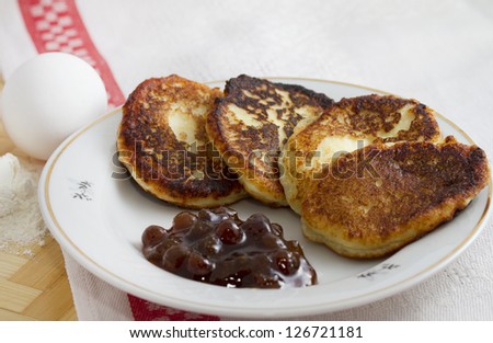 Curd pancake on a plate with strawberry jam and a handful of flour and egg
