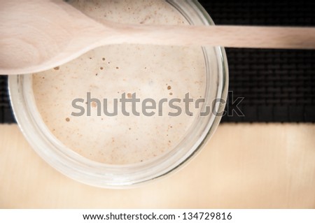Sourdough in a jar with wooden spoon on top on wood table with a dark table mat
