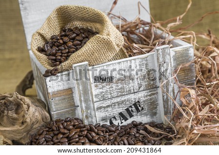scattered roasted coffee beans in front of old wooden box with a burlap bag filled with coffee beans