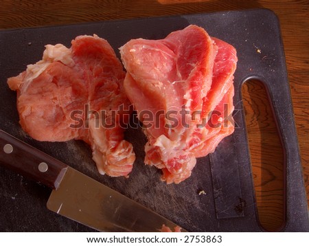 Crude meat on a chopping board and a knife.