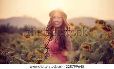 A happiness woman wear hat and pink dress in sunflower fields with filtered warm tone and sun flare.