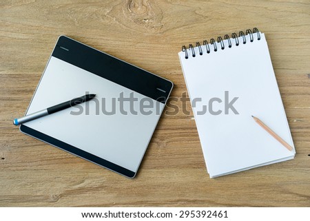 Blank modern digital tablet digitizer with blank note and pencil objects on a wooden desk in Top view with vintage grainy instagram filtered.