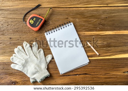 Blank note papers cutter cotton glove measure tape and pencil objects on a wooden desk in Top view.