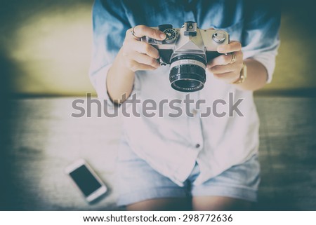 Woman holding vintage film camera and put smartphone on side with vintage color filter and vignette.