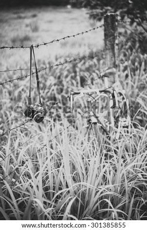 Vintage film camera and bicycle park with rust barbed wire in black and white filter.