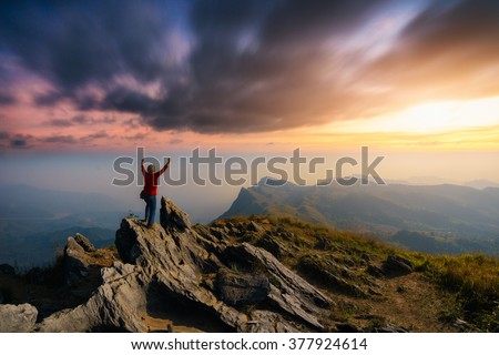 Successful journey man raising arms and stand on top of mountain peak with beautiful sunset landscape. Outdoor lifestyle and Business successful concept.