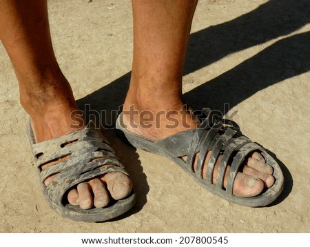 dirty male feet in rubber slippers on dried earth