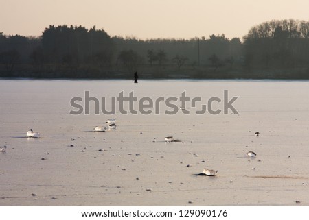 Ice lake with two men fishing under ice in the back ground