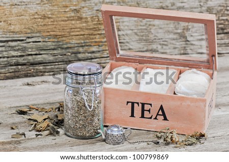 Loose tea in a jar and tea bags in a box with a tea strainer on a barn board background.