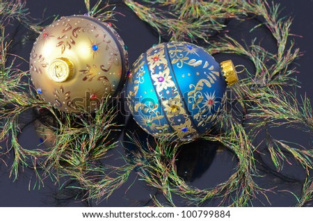 Two ornamental Christmas Balls on a black reflective background with iridescent eyelash ribbon.