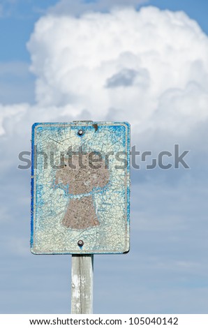 A weathered road sign against a cloudy sky
