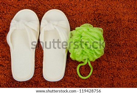 Organic Bamboo slippers on a rust colored bath mat with a green mesh body scrubber