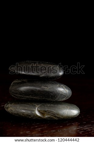 Three smooth stones balanced on a rich wood surface with a dark background