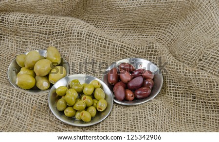 Three types of pickled olives in stainless steel dishes on a burlap background