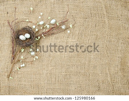 A spring or Easter branch crafted from a nest, eggs, willow and twigs on a burlap background with room for text