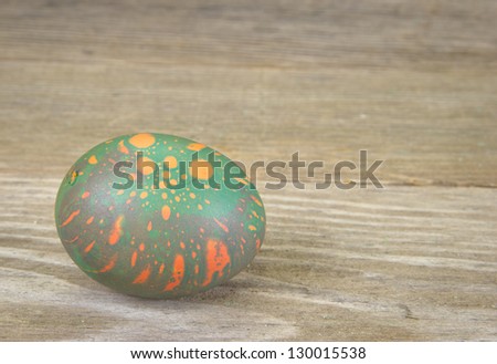 An orange and green colored Easter egg on an aged wood surface