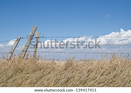 Three fence posts and barbed wire fence with cloudy blue prairie sky