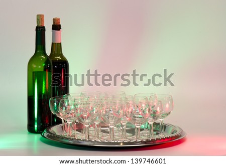 Wine bottles and tray of empty wine glasses with red and green accent lighting