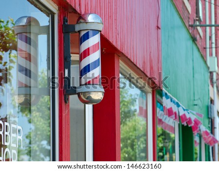 Barber pole on a red and green building with red white and blue banner behind.