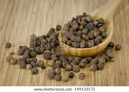 Whole allspice seeds on a bamboo spoon and cutting board