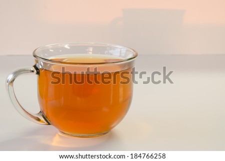 A clear glass cup of  tea with a cinnamon stick and star anise on a reflective surface
